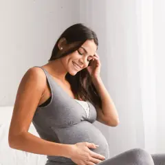 Mujer sonríe mientras acaricia su vientre en avanzado embarazo. Siente el hipo del bebé, un dulce anticipo de la vida.
