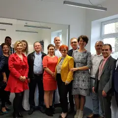 Grupa ludzi w eleganckich strojach pozuje do zdjęcia w biurze.