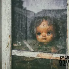 Przerażająca lalka Annabell spogląda przez brudne okno starego domu.