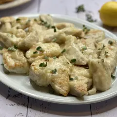 Delizioso pollo al limone ricetta, servito su un piatto bianco con erbe aromatiche e un limone sullo sfondo.