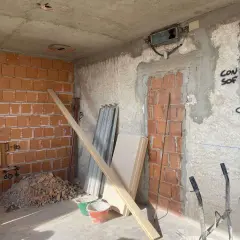 Interno di una casa in fase di ristrutturazione: pareti in mattoni a vista, cumulo di macerie, secchi, assi di legno e materiale edile.