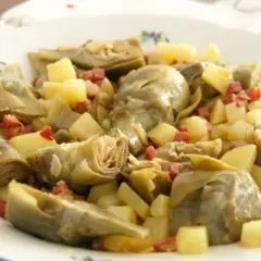Plato de alcachofas tiernas y patatas cortadas en cubos, salpicado con trocitos de jamón. Un manjar casero.