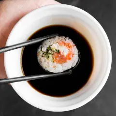 Pałeczkami zanurzam rolkę sushi z łososiem w ciemnym sosie.