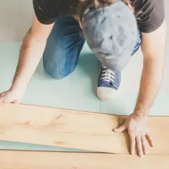 Uomo posa pannelli per come isolare il pavimento dal freddo. Sottile strato isolante azzurro sotto le assi di legno.