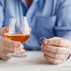 Mężczyzna trzyma kieliszek z alkoholem i obrączkę. Rozważania o rozdzielności majątkowej a alimentach na dziecko z poprzedniego związku.
