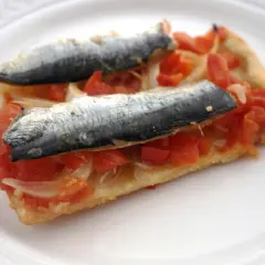 Rebanada de masa con tomate, cebolla y dos sardinas enteras, un plato que recuerda a las sardinas San Juan.