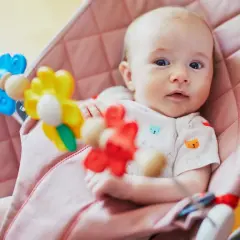 Söt bebis i en rosa babysitter vagga med färgglada leksaker.