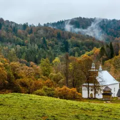Cerkiew w Łopience otoczona jesiennym lasem, mgła unosi się nad wzgórzami.
