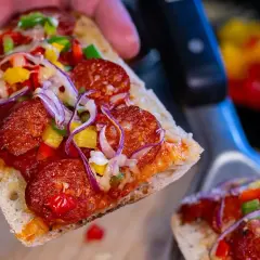 Pyszna zapiekanka z chorizo, papryką i cebulą, trzymana w dłoni.