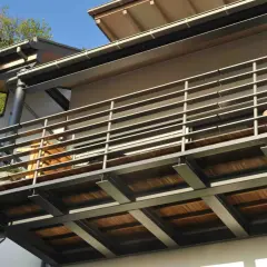 Nowoczesny rodzaj balkonu z drewnianym tarasem i metalową balustradą, wsparty na solidnych słupach.