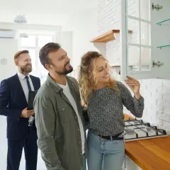 Couple inspecte une cuisine lors d'un état des lieux avant signature notaire. Un agent immobilier les accompagne.