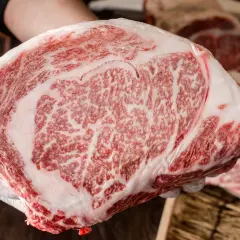 Ręka w białej rękawiczce trzyma kawałek soczystej wołowiny krowy wagyu z charakterystycznym marmurkowym przerostem tłuszczu.