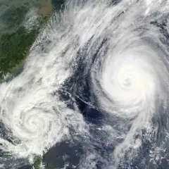 Dwa potężne wiry chmur, niczym oczy cyklonu, tworzą groźny **tajfun** nad oceanem, zbliżając się do zielonego wybrzeża.