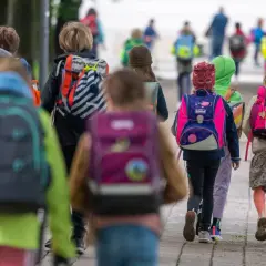 Kinder mit bunten Schulranzen gehen gemeinsam auf dem Weg zur Grundschule. Ein sicherer Schulweg ist wichtig für alle.