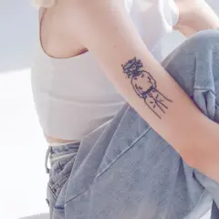 Ein Arm mit einem abstrakten Tattoo, das eine Figur mit einem Kranz darstellt. Die Linien sind klar und dick, ein typisches Merkmal für ein tattoo dicke linien.