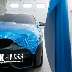 Oklejanie podsufitki samochodu folią w kolorze niebieskim. W tle widać auto częściowo zakryte folią.