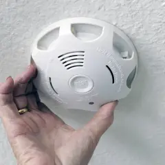 Ein weißer Rauchmelder wird von einer Hand gehalten. Er geht ohne Grund an und piept laut.