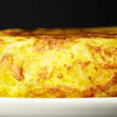 Złocista tortilla de patatas, pachnąca ziemniakami i jajkami, kusi apetycznym wyglądem na białym talerzu.