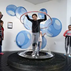 Barn utforskar vetenskap på 2047 science center, en flicka är innesluten i en gigantisk såpbubbla.