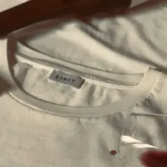 Un bouchon de liège et une bouteille de vin à côté d'un tee shirt blanc, avec une tache de vin rouge.