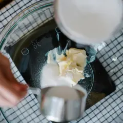 Kobieta wsypuje cukier do miski z masłem na wadze kuchennej.