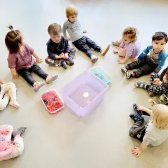 Dzieci siedzą w kółku na podłodze wokół pojemników z wodą i zabawkami.