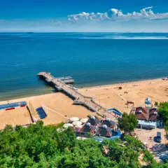 Piękny dzień na plaży w Polsce. Molo wchodzi w głąb morza, a piasek jest pełen ludzi cieszących się wakacjami.