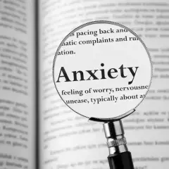 Lupa powiększa słowo "Anxiety" (lęki po angielsku) w książce, podkreślając definicję: "uczucie zmartwienia, nerwowości, niepokoju".