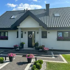Nowoczesny dom z kamiennymi elementami, piękne kwiaty przed wejściem. Koszty budowy takiego domu mogą być różne.
