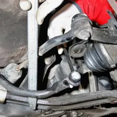 Montaż łącznika stabilizatora Toyota Yaris 1. Widoczna ręka w rękawiczce przykręca element zawieszenia.