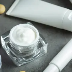 Crema blanca en un frasco de cristal, tubos y bolitas doradas. Descubre qué es el pantenol y sus beneficios para tu piel.