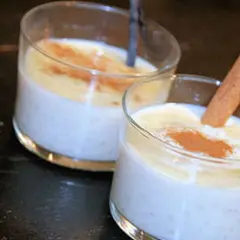 Deux verres de riz au lait crémeux, saupoudrés de cannelle. Un bâton de cannelle décore l'un des desserts, parfait pour une recette de riz au lait.