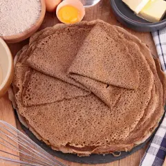 Pile de crêpes de sarrasin, avec des ingrédients pour la pâte à crêpe sarrasin : farine, œufs, beurre.