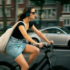 Frau fährt Fahrrad mit Kopfhörern und Tasche. Ob man mit AirPods Fahrrad fahren darf, ist eine Frage der Sicherheit und des Gehörs.