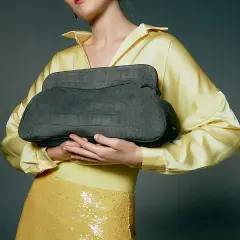 Elegante bolso gris de piel de cocodrilo, un accesorio de lujo de marcas españolas, sostenido por una mujer con blusa amarilla satinada y falda de lentejuelas.
