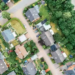 Widok z lotu ptaka na osiedle domów jednorodzinnych z ogrodami. Widać, ile budynek gospodarczy od granicy działki, drzewa i drogi.