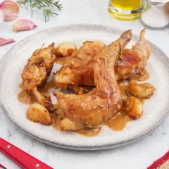 Delicioso conejo al ajillo servido en un plato, con ajos enteros y romero. Una receta tradicional lista para disfrutar.
