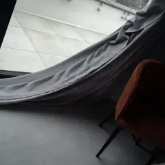 Szare zasłony swobodnie opadają na podłogę, tworząc przytulną atmosferę wokół pomarańczowego fotela.