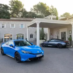 Dwa sportowe samochody, niebieski i grafitowy, zaparkowane przed luksusowym hotelem. Nowy Honda Prelude w niebieskim kolorze przyciąga wzrok.