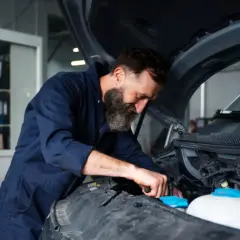 Mechanik z brodą pracuje przy silniku. Zastanawiasz się, ile kosztuje wymiana chłodnicy w samochodzie?