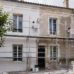 Ravalement de façade en cours, transformant une vieille bâtisse pour une plus-value certaine. Les ouvriers travaillent sur des échafaudages.