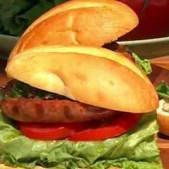 Sandwich de salchicha con lechuga, tomate y salsa chimichurri, con sus ingredientes frescos listos para servir.