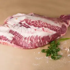 Un corte de carne cruda, con grasa marmoleada, listo para convertirse en un delicioso pastrami que es. Acompañado de perejil y ajos.