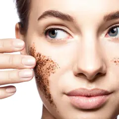 Une femme applique un gommage visage à base de grains de café. Elle montre comment faire un gommage visage pour une peau douce.