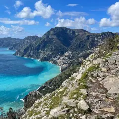Hikers on the "walk of the gods" trail, with stunning turquoise waters and coastal villages below.