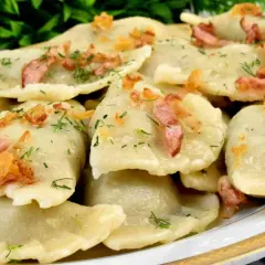Talerz pełen pysznych, domowych pierogów z młodej kapusty, posypanych skwarkami i koperkiem.