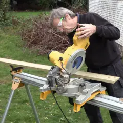 Man med skyddsglasögon använder en kap- och geringssåg för att kapa en träplanka. Olika sågar kan vara användbara för olika projekt.