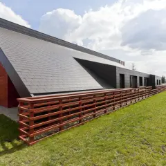 Nowoczesny budynek z dachówką struktonit, drewnianym ogrodzeniem i zielonym trawnikiem.