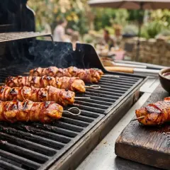 Fleischspieße mit Speck umwickelt brutzeln auf dem Grill. Perfekt für leckere Grill Rezepte im Sommer.