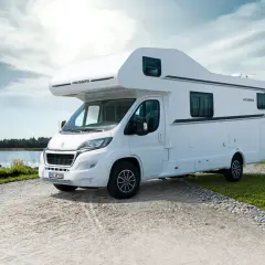 Biały kamper Weinsberg zaparkowany nad jeziorem, gotowy na przygodę. Ten camper to wolność podróżowania.